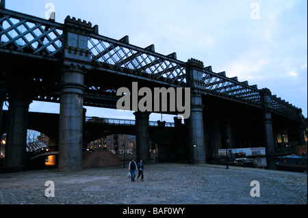 Couple walking by historic old industrial railway bridge over the Bridgewater canal,Castlefield,Manchester,evening Stock Photo