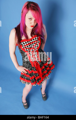 Full length Portrait of a beautiful teen girl with long pink hair pale skin and red lips wearing a red and black dress. Stock Photo