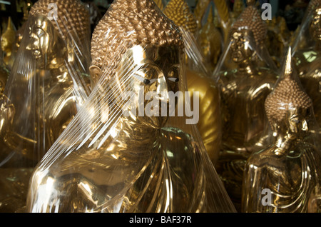 Plastic shrouded Buddha images sit in a shop awaiting enshrinement in a one of the many temples in Bangkok Thailand Stock Photo