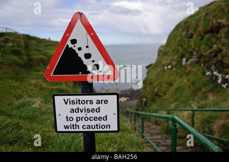 Falling rocks sign on a path beside a seaside cliff warning 'Visitors are advised to proceed with caution' Stock Photo