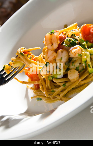 Gourmet Seafood Linguine with tiger shrimp and oven roasted tomatoes and zucchini being lifted by a fork. Stock Photo