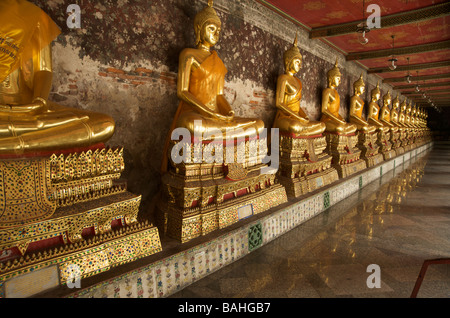 Gold Buddha statues line the galleries that encircle the main building at Wat Suthat in Bangkok Thailand Stock Photo