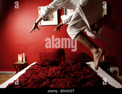 man in bathrobe jumping into his red bed Stock Photo