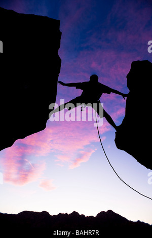 A climber is silhouetted as he reaches across a gap in the rock in the Sierra Nevada Mountains California Stock Photo