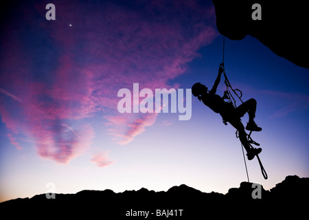 A climber dangles in midair as she rappels from the summit of a rock spire Stock Photo