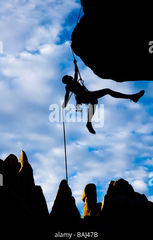 A climber dangles in midair as she rappels from the summit of a rock spire in The Sierra Nevada Mountains California Stock Photo