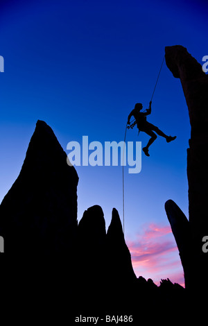 A climber is silhouetted as she rappels from the summit of a rock spire Stock Photo
