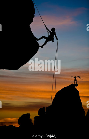 A climber is silhouetted as she rappels from the summit of a rock spire. Stock Photo