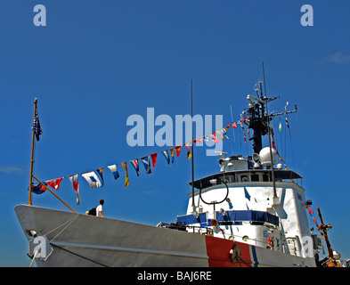 US Coast Guard cutter at dock with bright red and blue highlights on white with communication tower and pennants blue sky Stock Photo