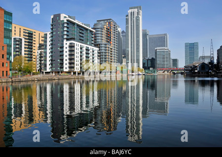 East London Docklands waterside housing in high rise apartments flats development water reflections Millwall Docks Canary Wharf & DLR train beyond UK Stock Photo