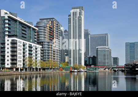 East London Docklands waterside housing in high rise apartments flats development water reflections Millwall Docks Canary Wharf & DLR train beyond UK Stock Photo