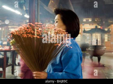 WOMAN HOLDING BIG BUNCH OF INCENSE STICKS IN BUDDHIST TEMPLE IN TAIWAN Stock Photo