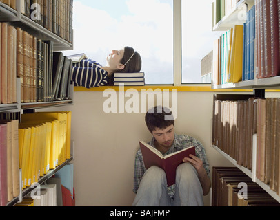 Female student lying down on library windowsill, male student sitting on library floor reading Stock Photo