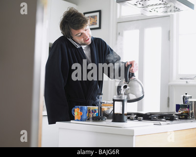 Man standing in kitchen using phone, pouring water into coffee plunger Stock Photo