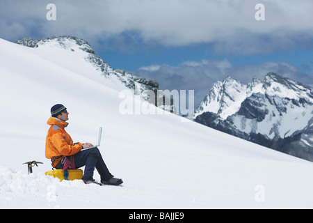 Hiker using laptop on snowy mountain peak Stock Photo