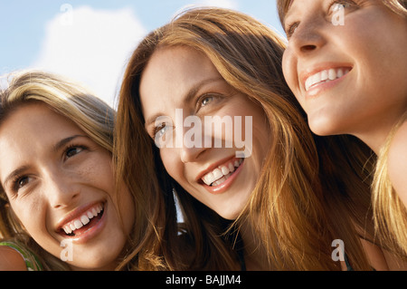 Three young women sitting side by side looking at view, close up, head and shoulders Stock Photo