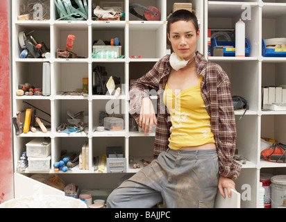 Young Woman leaning on Tool Shelves, portrait Stock Photo