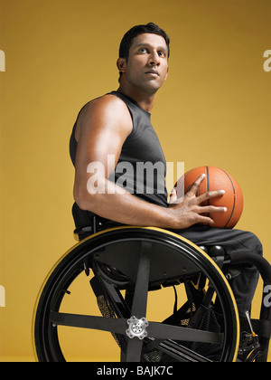 Paraplegic athlete sitting in wheelchair holding basketball, side view