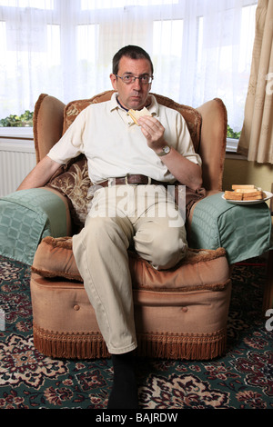 A one legged paraplegic sits in an armchair eating sandwiches at lunchtime Stock Photo