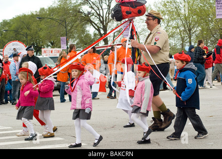 Youn girls and boys in scout uniforms and ladybug berets hold on to streamers of maypole and march in Chicago Polish Parade Stock Photo