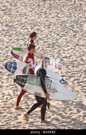 Three surfers with their surf boards exiting the water in Huntington Beach, California Stock Photo