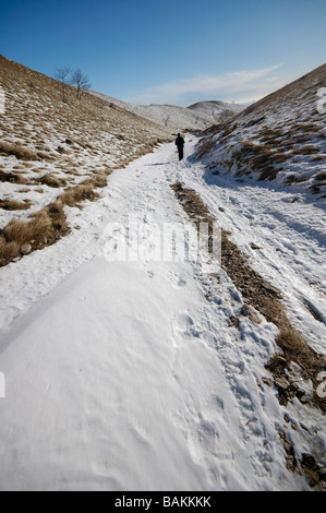 Man on a pathway in a mountain, covered with snow during bright sunny day Stock Photo