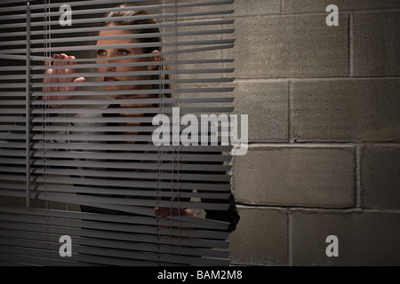 Woman looking through blinds Stock Photo