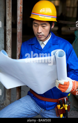 Man In Construction Site Wearing A Hard Hat And Holding Blueprints Stock Photo