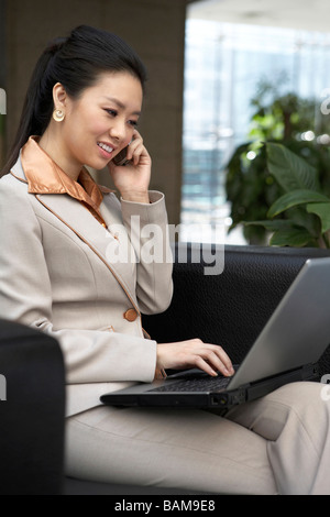 Businesswoman Typing On Laptop, Talking On Cellphone Stock Photo