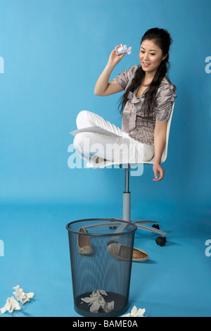 Woman Sitting On Chair, Throwing Paper Into Bin Stock Photo