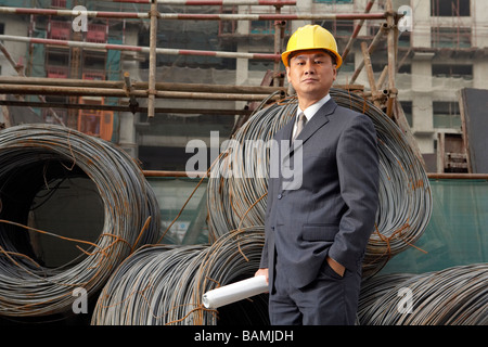 Businessman In A Construction Site Wearing A Hard Hat And Holding Plans Stock Photo