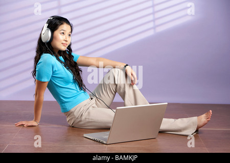 Woman Sitting On Floor With Computer Wearing Headphones Stock Photo