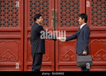 Two Businessmen Shaking Hands In Doorway Of The Forbidden City In Beijing Stock Photo