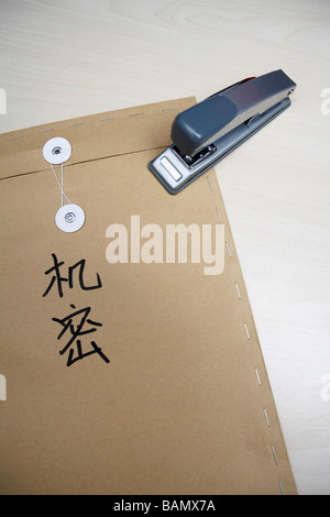 A stapler resting on a brown envelope that has 'top secret' in Chinese characters written on it Stock Photo