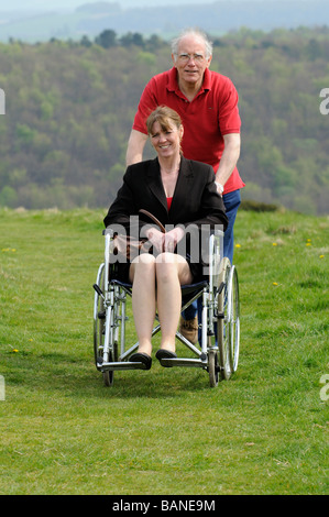 Carer pushing woman in a wheelchair in the English countryside UK Stock Photo