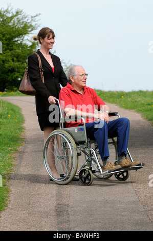 Female carer pushing elderly man in a wheelchair in the English countryside UK Stock Photo