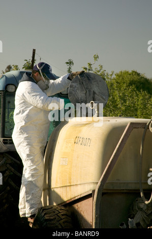 Farmer adding chemicals into spray rig wearing protective clothing. Stock Photo