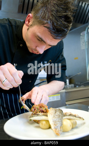 A chef putting the finishing touches to a fish dish in the kitchen of a small restaurant Stock Photo
