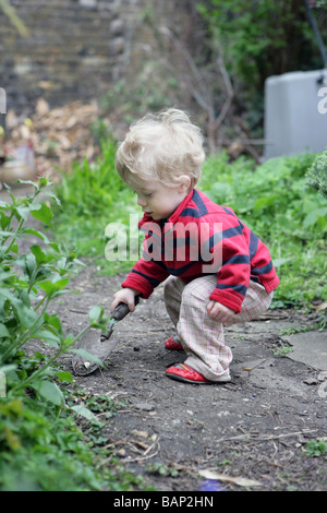 eighteen month old plays with a trowel in a North London garden Stock Photo