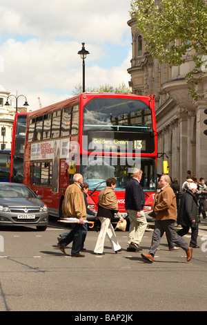 Central London pedestrians cross the busy Strand road with a London red double decker bus behind Stock Photo