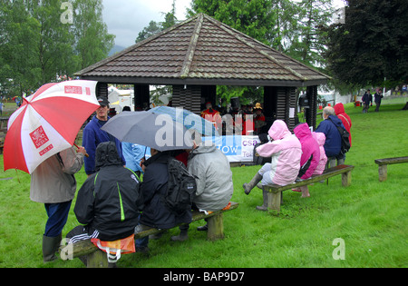 Audience sitting on benches under umberellas to listen to brass band play in  covered bandstand in the rain at Royal Welsh Show Stock Photo