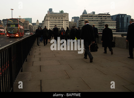 Commuters walking over London Bridge in the morning, with a red London bus on the road. Stock Photo