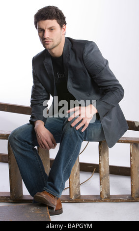 Studio shot of man in casual clothes , sitting on steps, fuul length Stock Photo