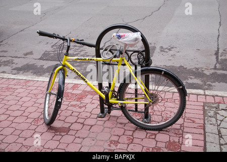 A bicycle locked to a bike rack with a bicycle lock The seat is covered with a plastic bag to protect it from the rain Stock Photo