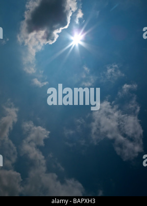 The sun appearing from behind a cloud in deep blue sky Stock Photo
