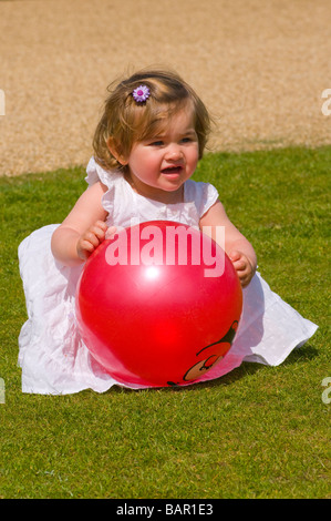 Young Girl Child Playing With a Red Plastic Ball In a Summer Dress Stock Photo
