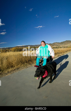 Woman uses her electric wheelchair to navigate the walking path in the small mountain town of Salida Colorado USA Stock Photo