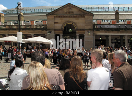 Crowds of tourists watching street artists busking in the sunshine outside Covent Garden Market in London. Stock Photo