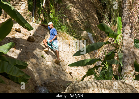 Omani Wakir is climbing up the terraced gardens to open the water channels from the ancient irrigation system Stock Photo