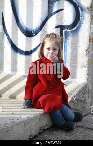 little girl in red coat sits on berlin wall segment sneezing